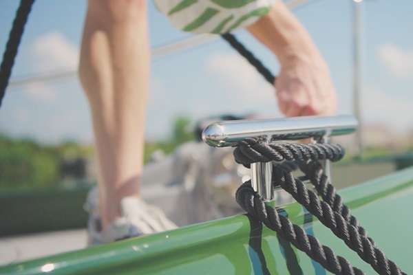 Close-up van een aanleglijn op een boot, met op de achtergrond een persoon in zomerse kleding die aan boord stapt bij zonnig weer.