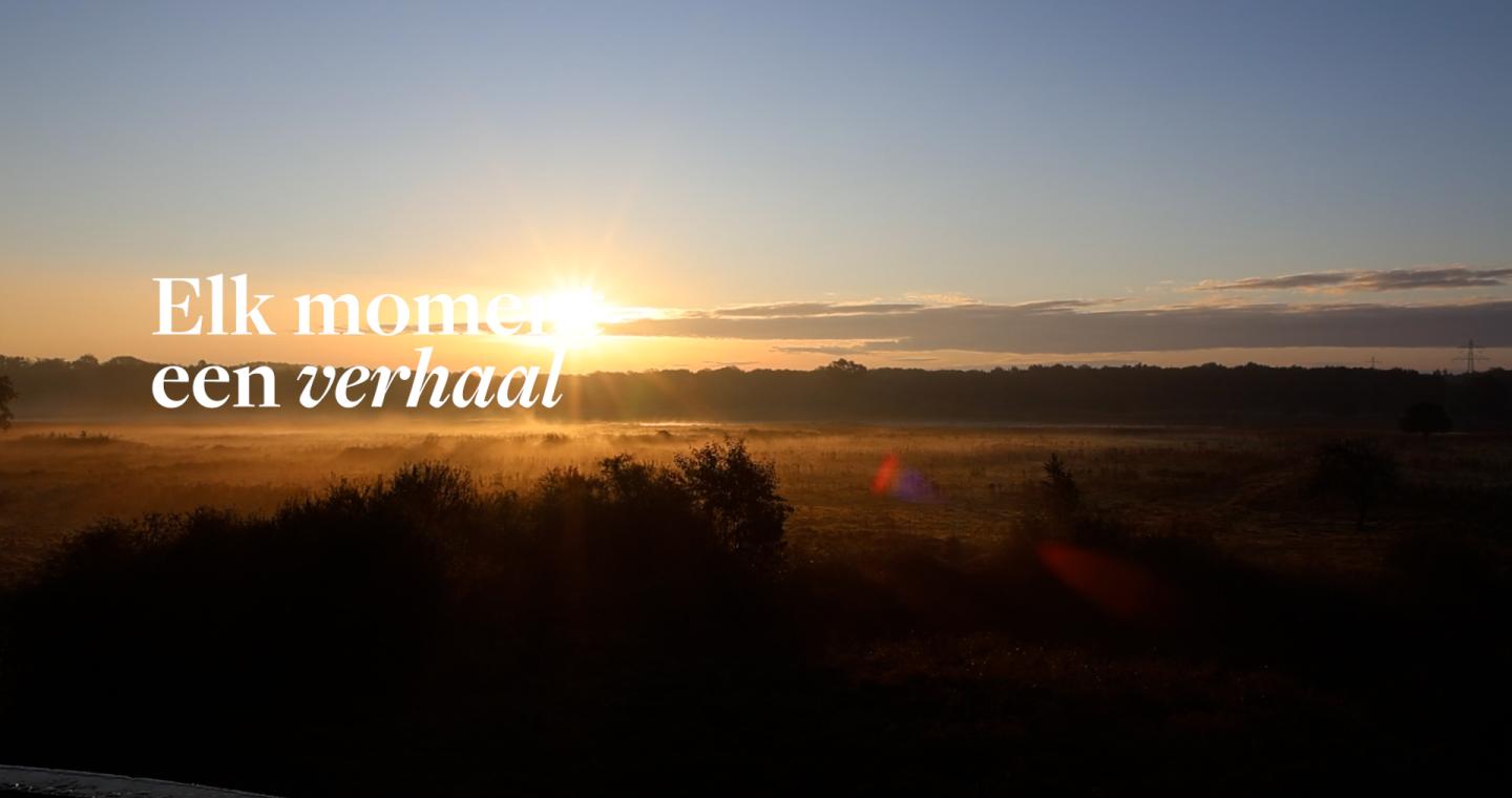 Zonsopkomst boven een nevelig landschap met de tekst ‘Elk moment een verhaal’ in beeld.