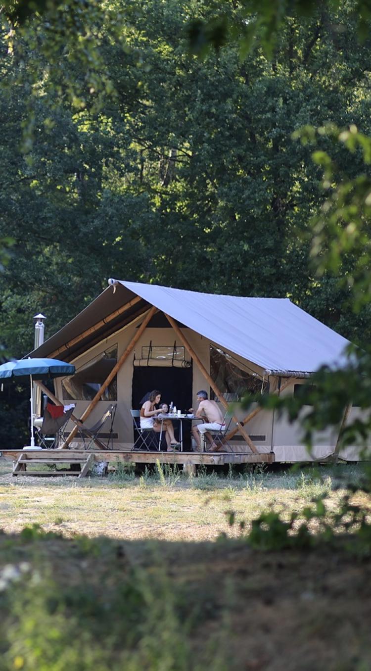Een gezin geniet van een zomers ontbijt voor hun safaritent tijdens het kamperen in Limburg, omringd door bos en ochtendzon.