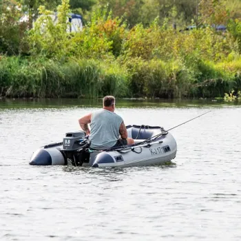 Een man zit in een rubberboot op de Maasplassen en vist rustig op open water, omringd door groen.