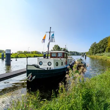 Historisches Boot liegt an einem Steg auf einem ruhigen Kanal inmitten grüner Natur.