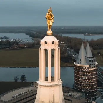 Gouden beeld van Sint Christoffel op de toren van de kathedraal in Roermond, met de Maas en de stad op de achtergrond.