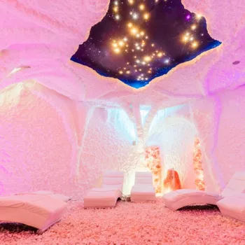 Zoutgrot met roze verlichte zoutwanden, ligstoelen en een sterrenhemel aan het plafond.